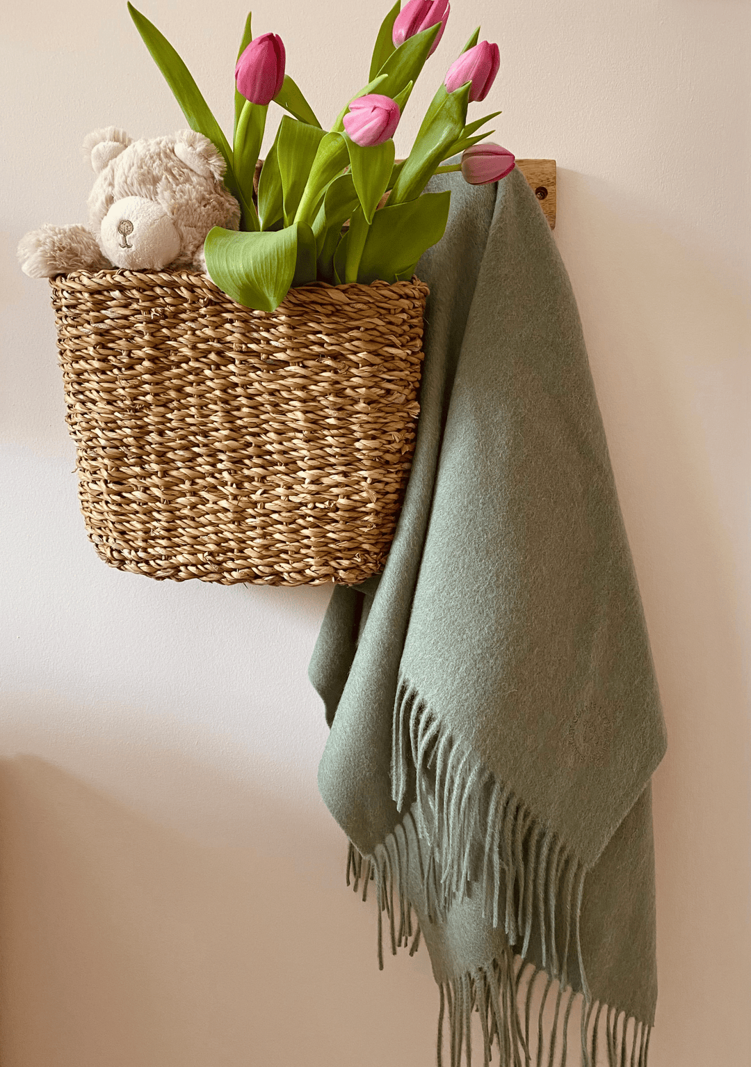 TBCo Lambswool Baby Blanket in Sage Melange displayed with pink tulips and teddy bear in woven basket on wall