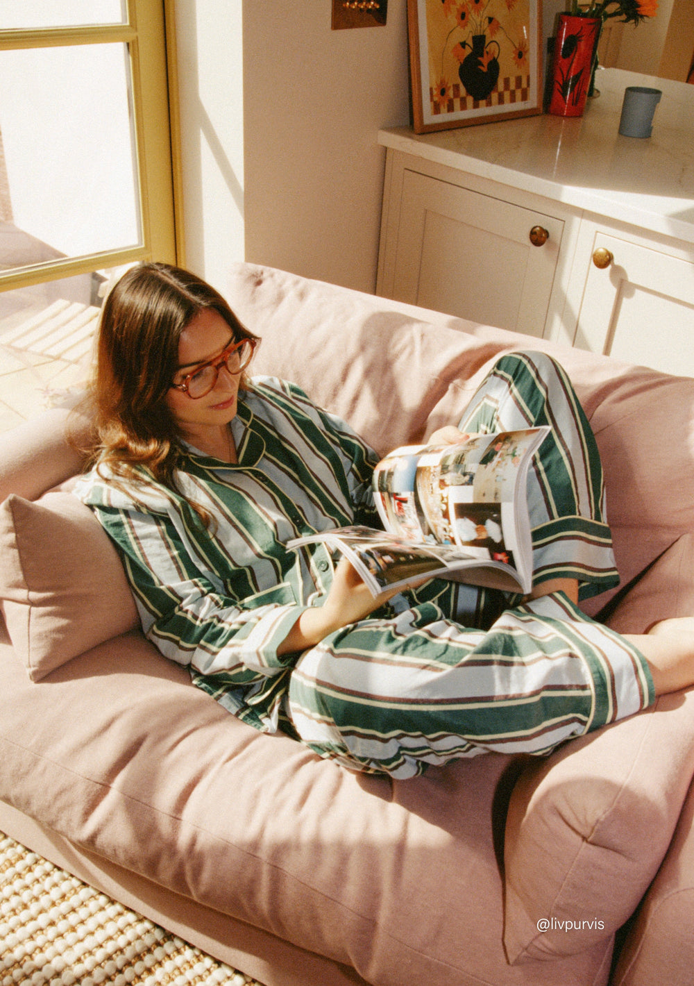Woman relaxing on a sofa reading a magazine wearing TBCo Cotton Pyjamas in Blue Stripe with tailored design