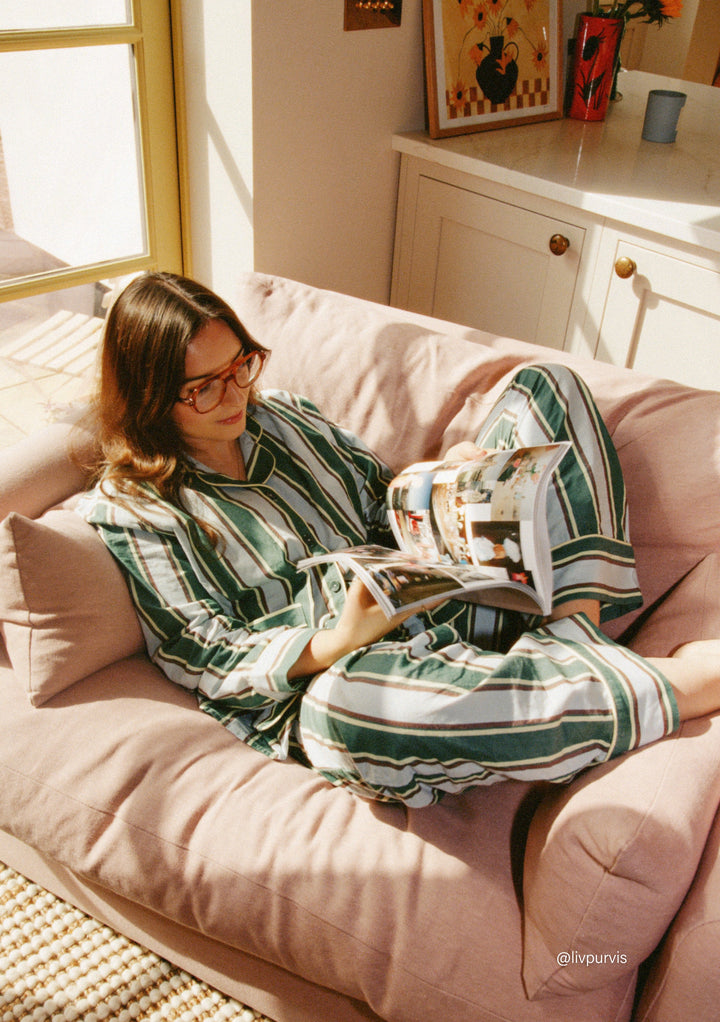 Woman relaxing on a sofa reading a magazine wearing TBCo Cotton Pyjamas in Blue Stripe with tailored design