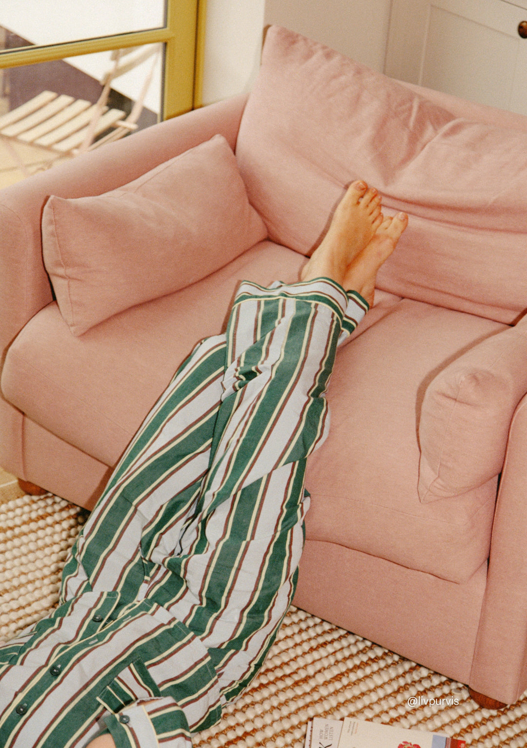 Relaxed person wearing TBCo Cotton Pyjamas in Blue Stripe lying on a soft pink sofa in a cosy home setting