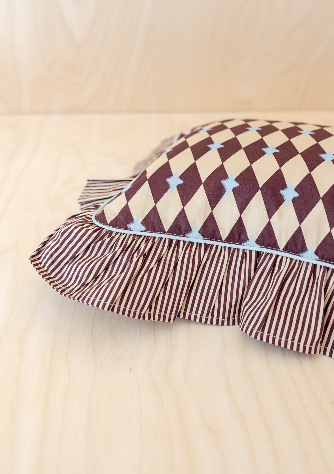 Close-up of TBCo Cotton Cushion Cover in Camel Harlequin with ruffled edge and contrasting stripe reverse design on wooden surface
