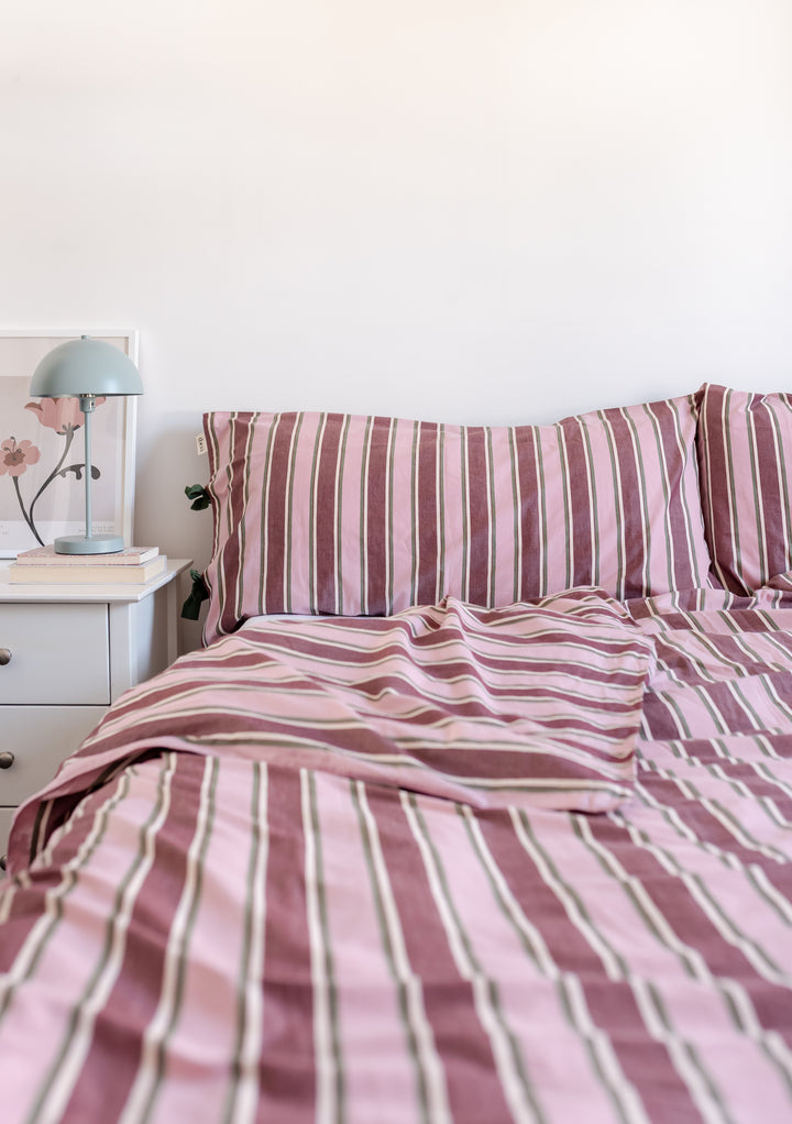 Cotton Duvet Cover in Pink Stripe by TBCo displayed on bed with matching pillowcases in softly lit bedroom.