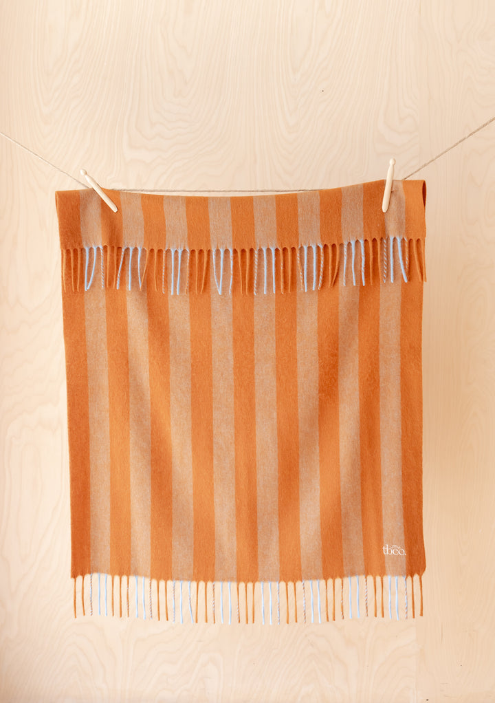 Lambswool Baby Blanket in Pumpkin & Blue Stripe by TBCo hanging with fringes in soft striped lambswool design