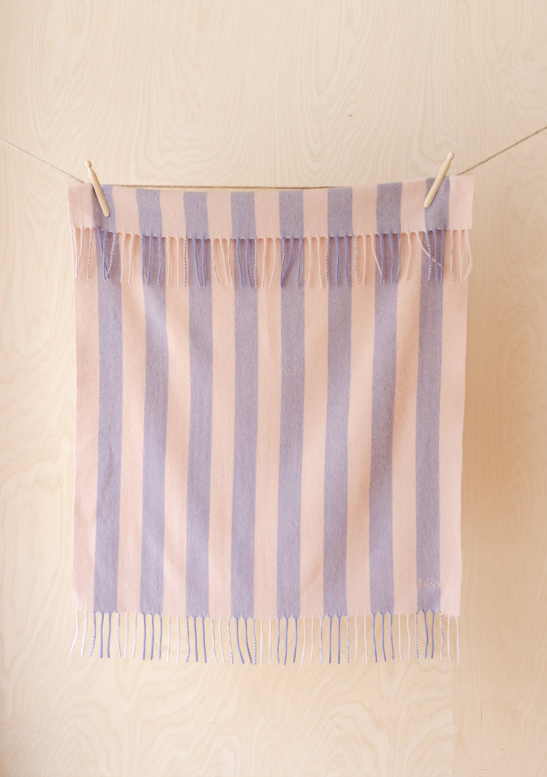 Lambswool Baby Blanket in Pink & Lilac Stripe by TBCo hanging with fringed edges on light wood background