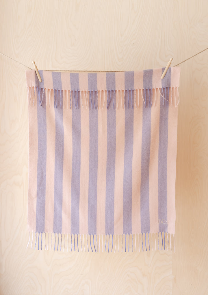 Lambswool Baby Blanket in Pink & Lilac Stripe by TBCo hanging with fringed edges on light wood background