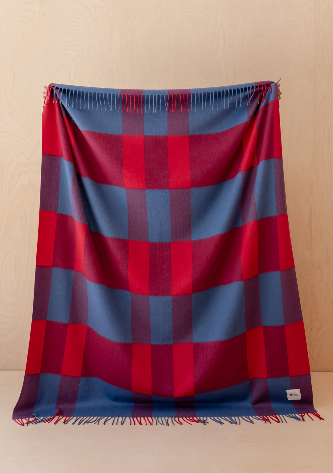 Lambswool Blanket in Red Modern Check by TBCo displayed hanging with fringed edges and vibrant wool fibre colors