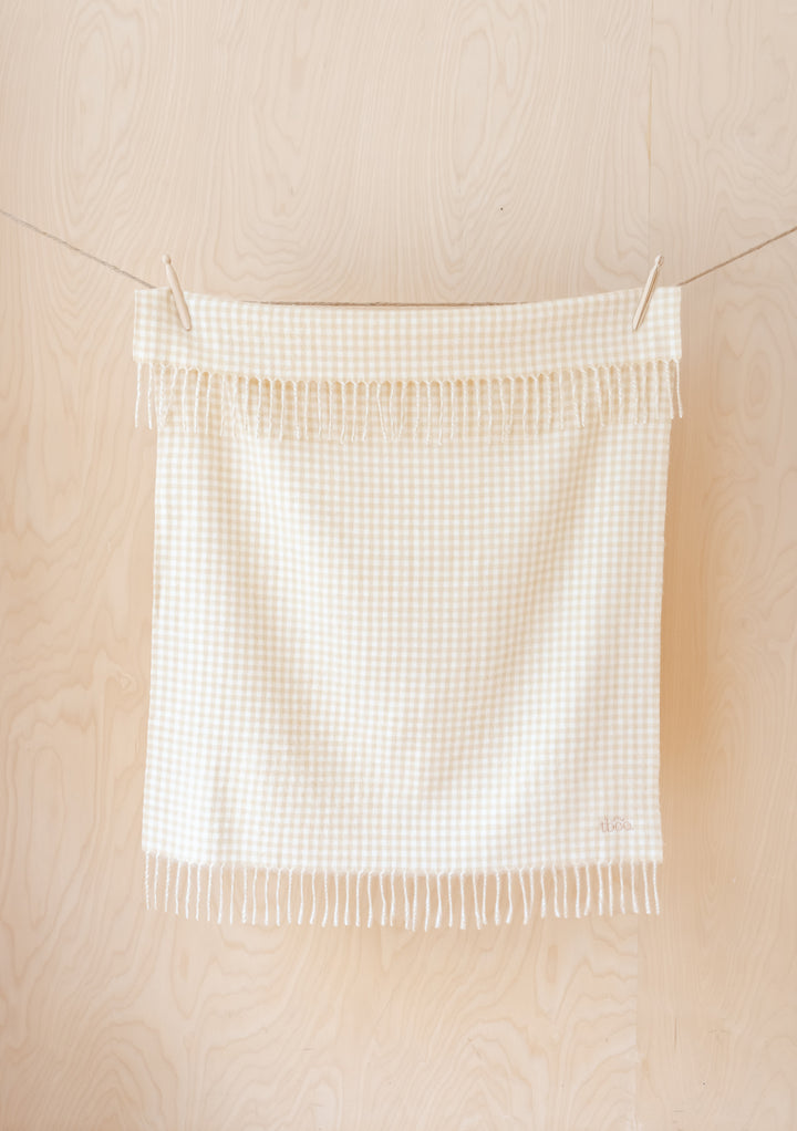 TBCo Lambswool Baby Blanket in Oatmeal Gingham hanging on clothesline, displaying fringed edges and micro check pattern