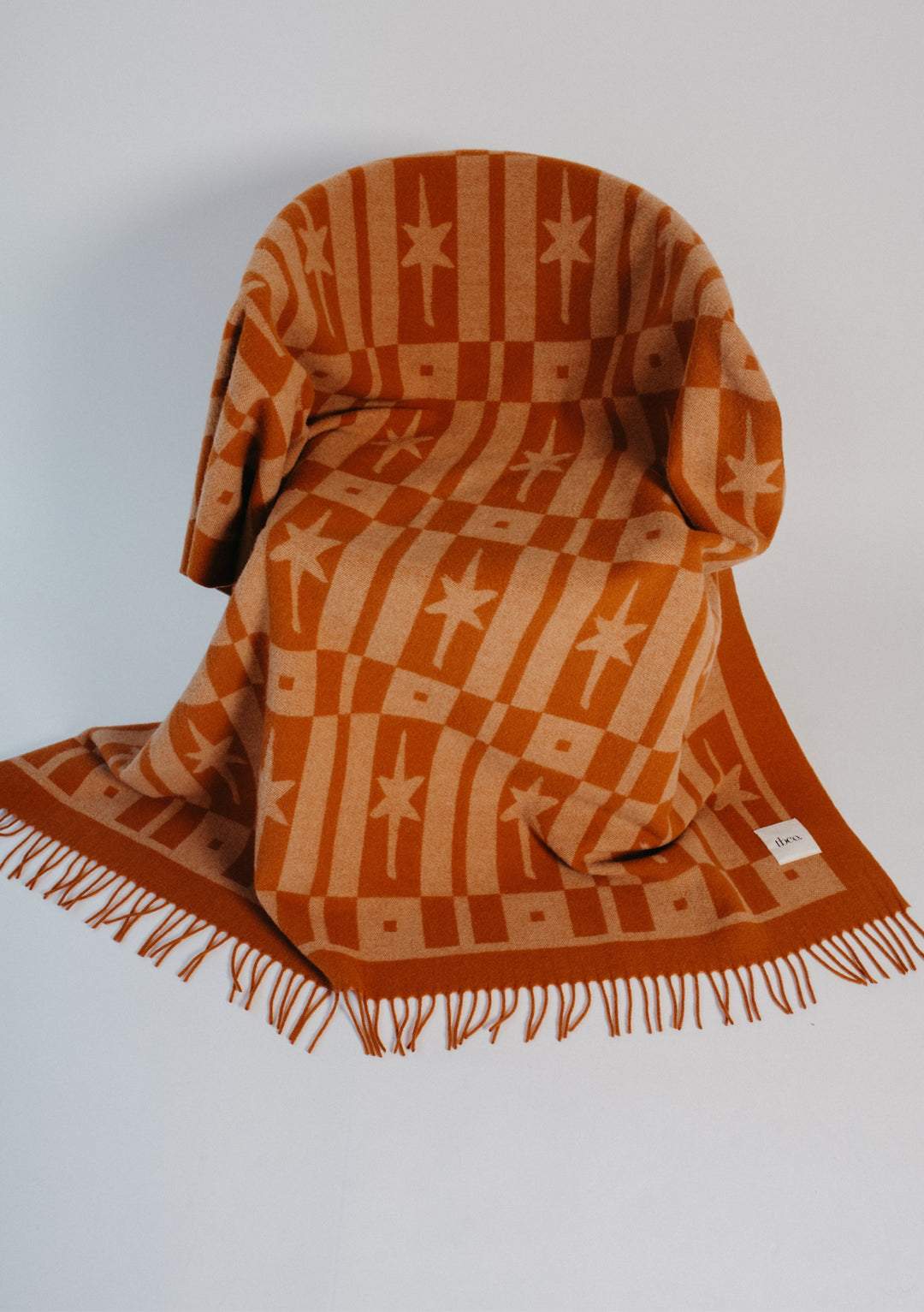 TBCo Lambswool Blanket in Almond Celestial Tile Jacquard draped over chair showing fringed edges and texture