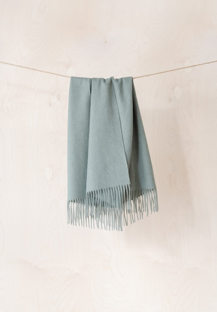 TBCo Lambswool Baby Blanket in Sage Melange hanging on rope, showing soft fringed edges and gentle draping
