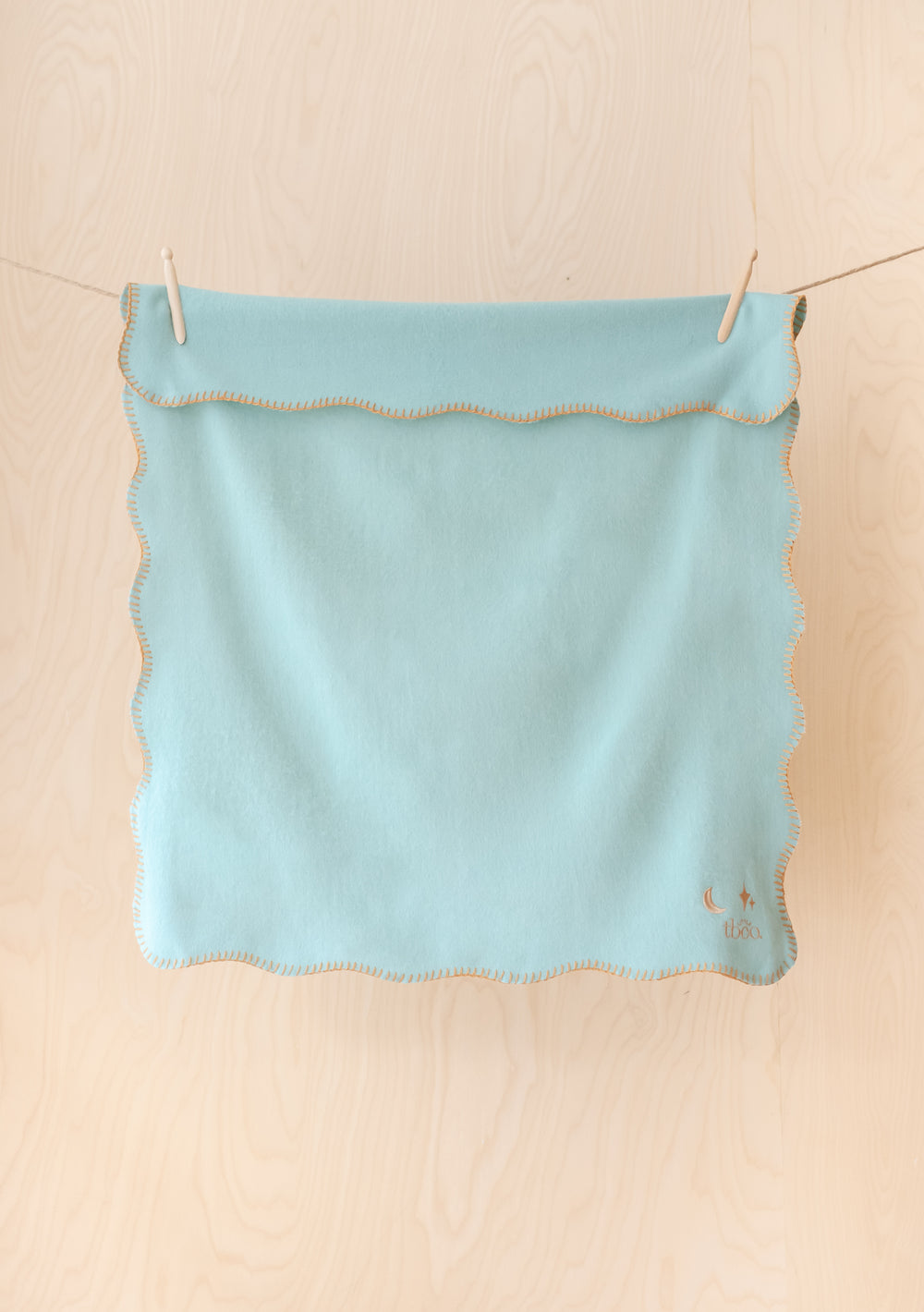 TBCo Lambswool Baby Blanket in mint green with tan scalloped edges and moon star embroidery, hanging on clothesline