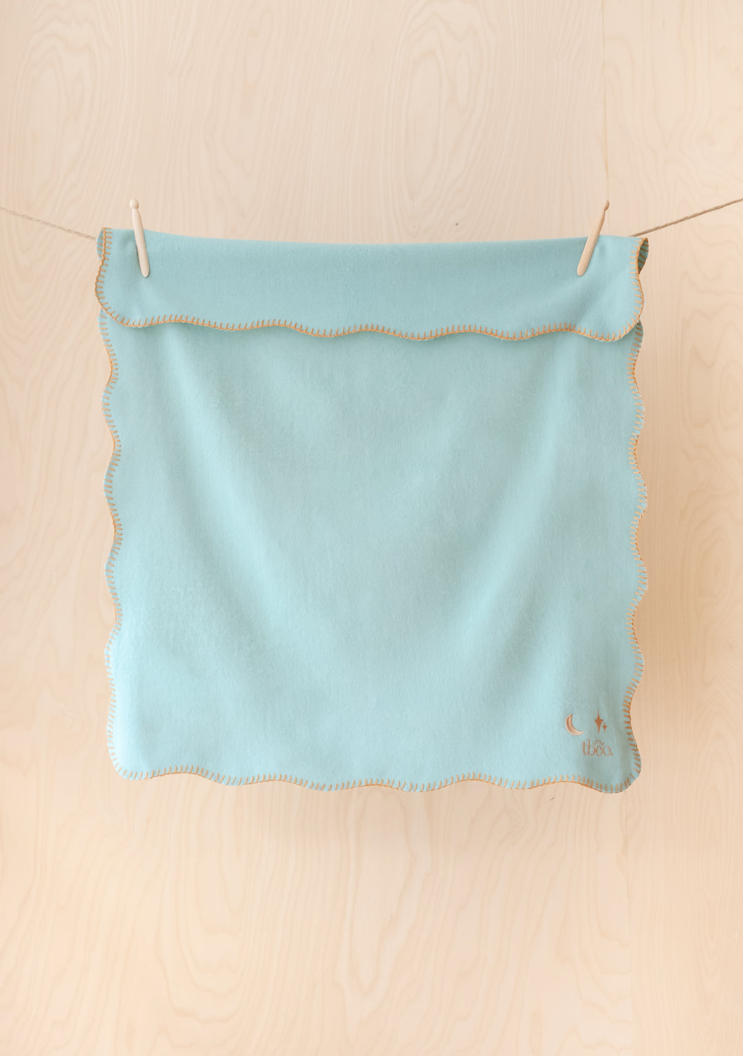 TBCo Lambswool Baby Blanket in mint green with tan scalloped edges and moon star embroidery, hanging on clothesline