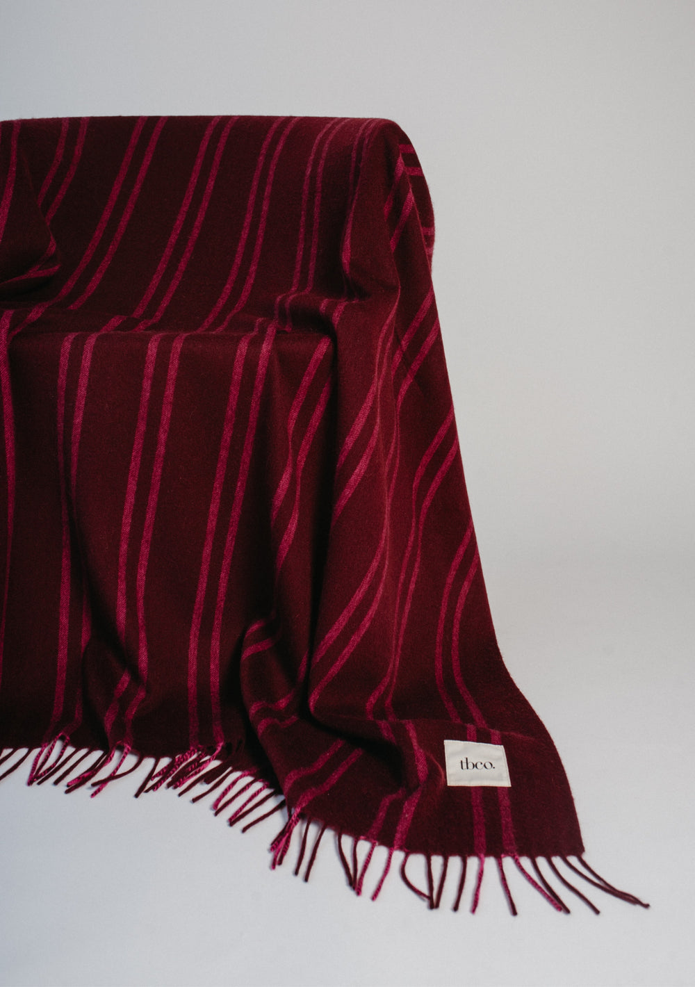 TBCo Lambswool Blanket in Wine Stripe draped softly showing fringed edge and subtle pink pinstripe design