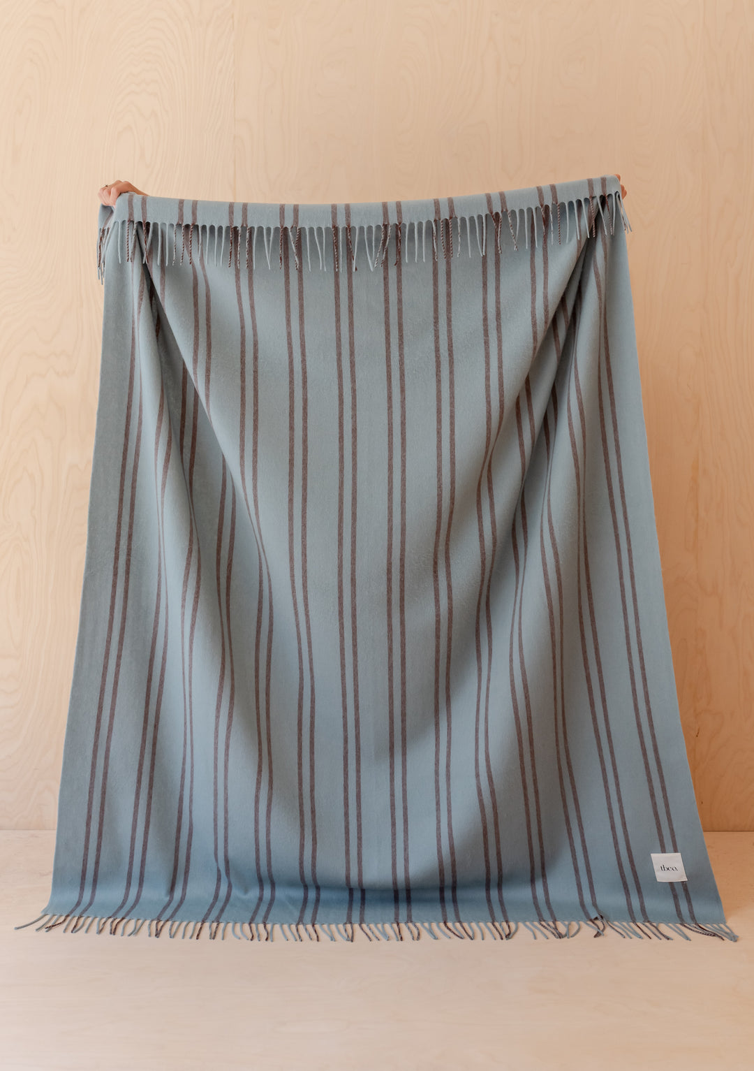 A person holding the TBCo Lambswool Blanket in Mint Stripe with brown pin stripes and fringed edges