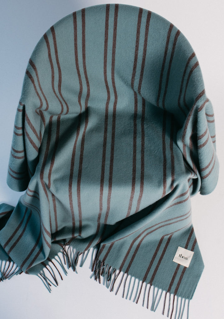 TBCo Lambswool Blanket in Mint Stripe draped elegantly with fringed edges showcasing soft blue with brown pin stripes