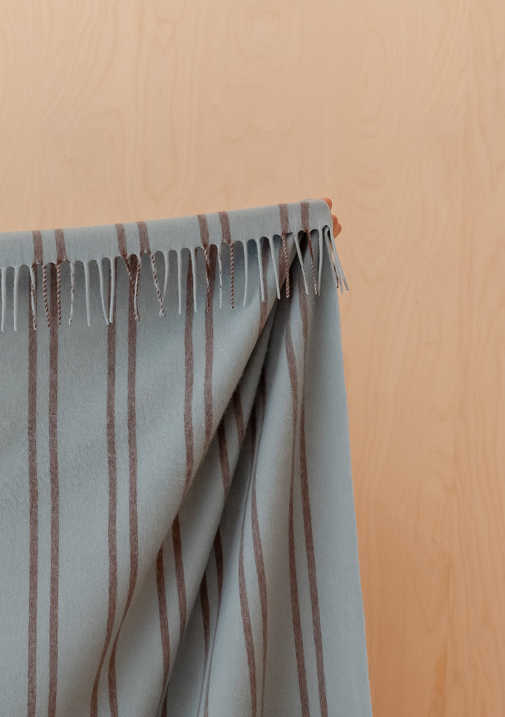 TBCo Lambswool Blanket in Mint Stripe with brown pin stripes and fringed edges draped against a wooden background