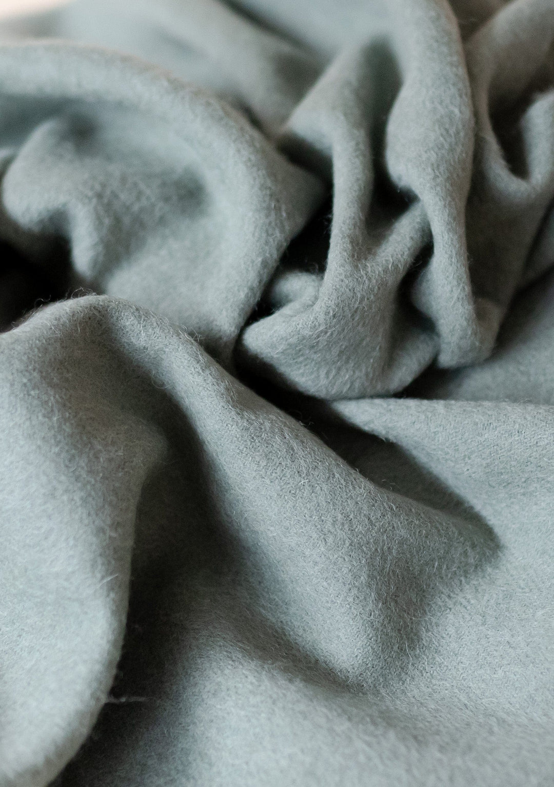 Close-up texture of TBCo's Lambswool Baby Blanket in Sage Melange showing soft, draped wool fabric with gentle folds