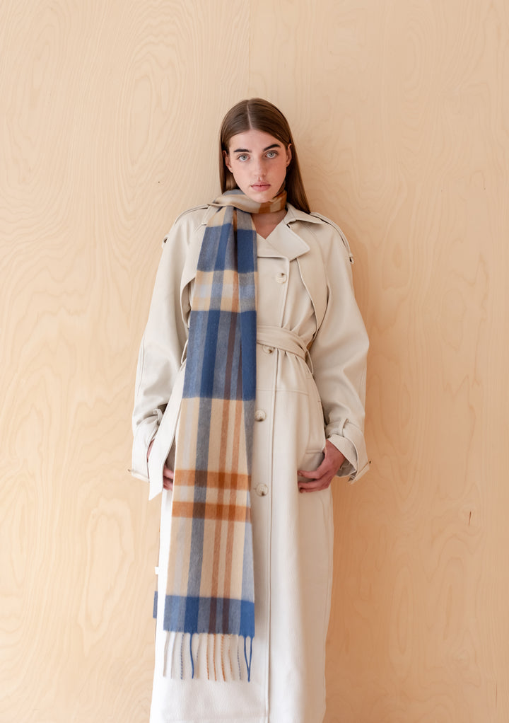 Model wearing TBCo Lambswool Skinny Scarf in Camel Modern Tartan with a light trench coat against wooden background