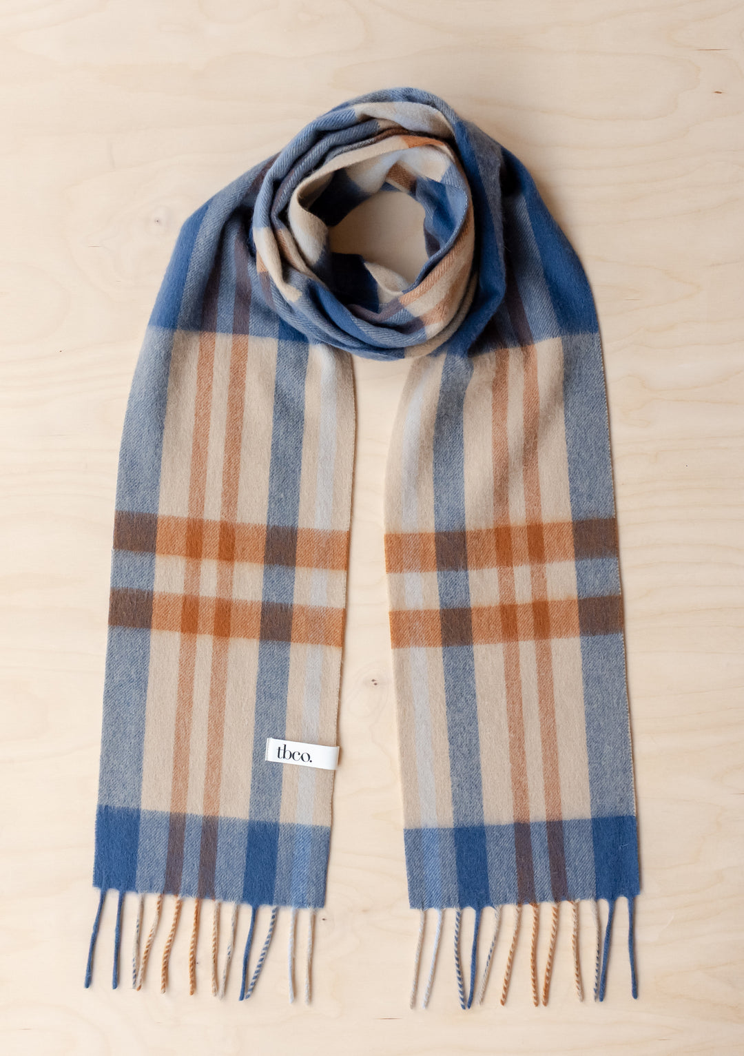 TBCo Lambswool Skinny Scarf in Camel Modern Tartan with blue and camel tartan pattern and fringed edges on wooden surface