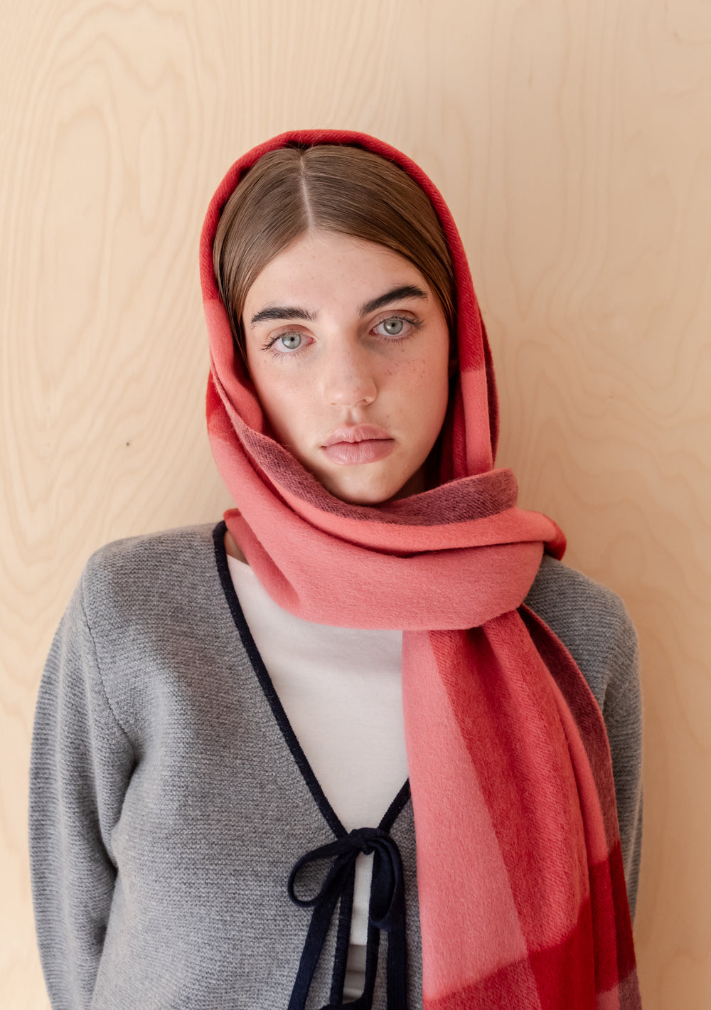 Woman wearing a TBCo Lambswool Oversized Scarf in Berry Block Check wrapped around head and neck against wood background