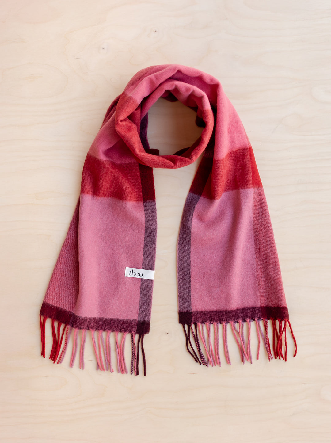 Lambswool Oversized Scarf in Berry Block Check by TBCo, soft and warm with fringed edges on wooden background