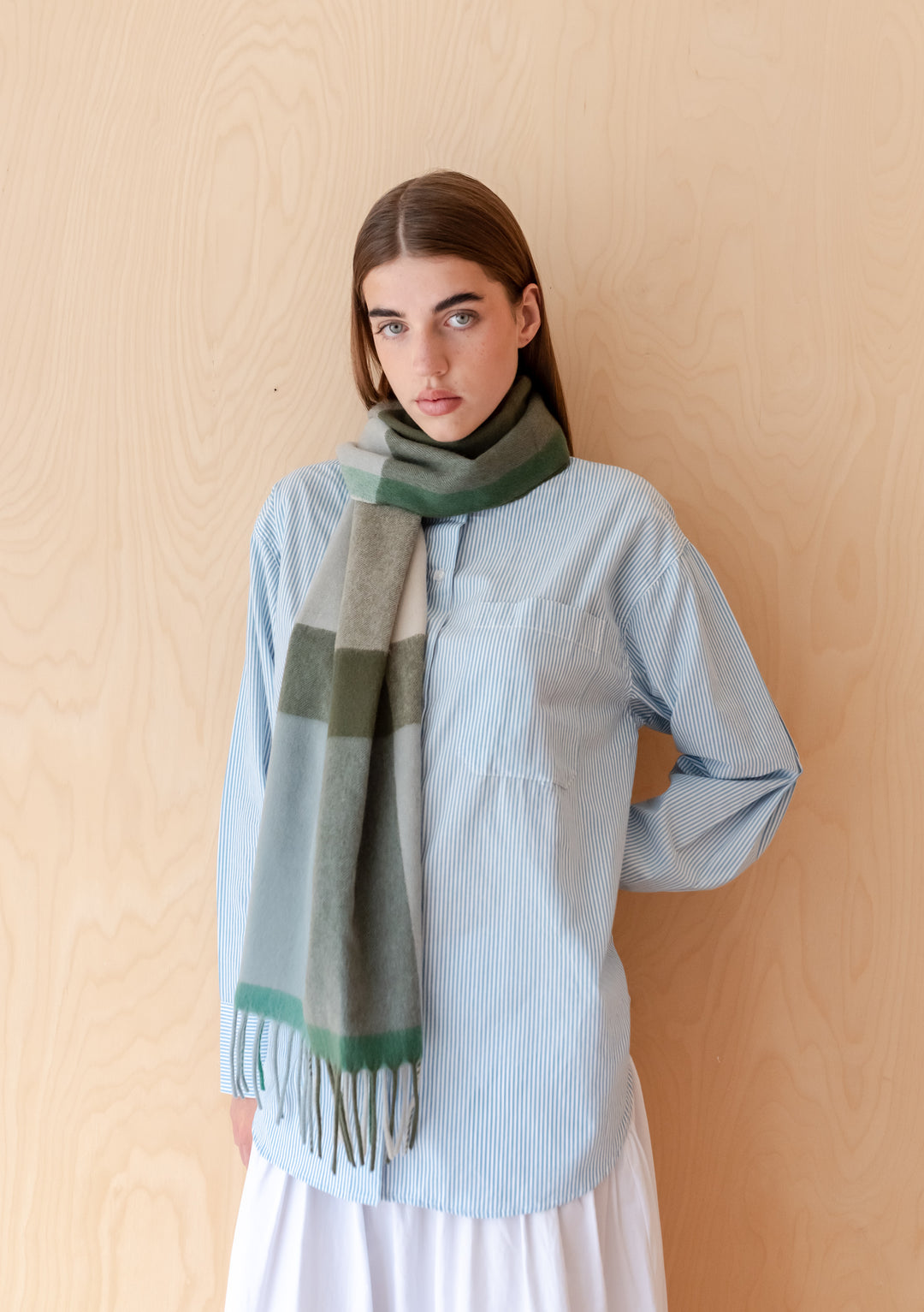 Model wearing TBCo Lambswool Oversized Scarf in Green Block Check with soft fringed edges against wooden background