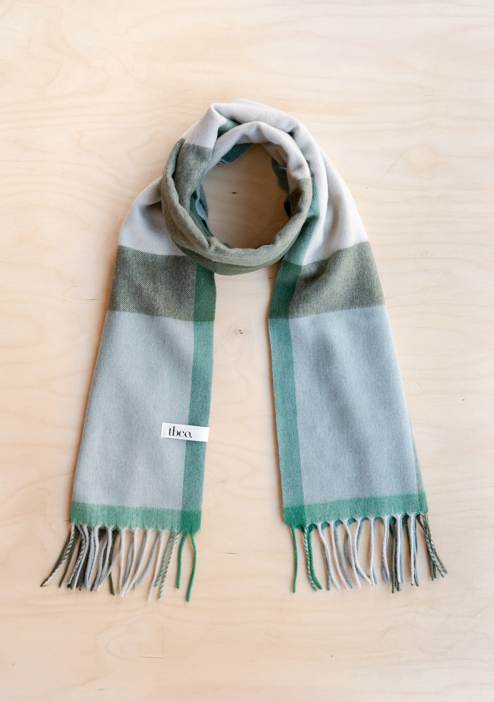 TBCo Lambswool Oversized Scarf in Green Block Check with fringed edges laid flat on wooden surface