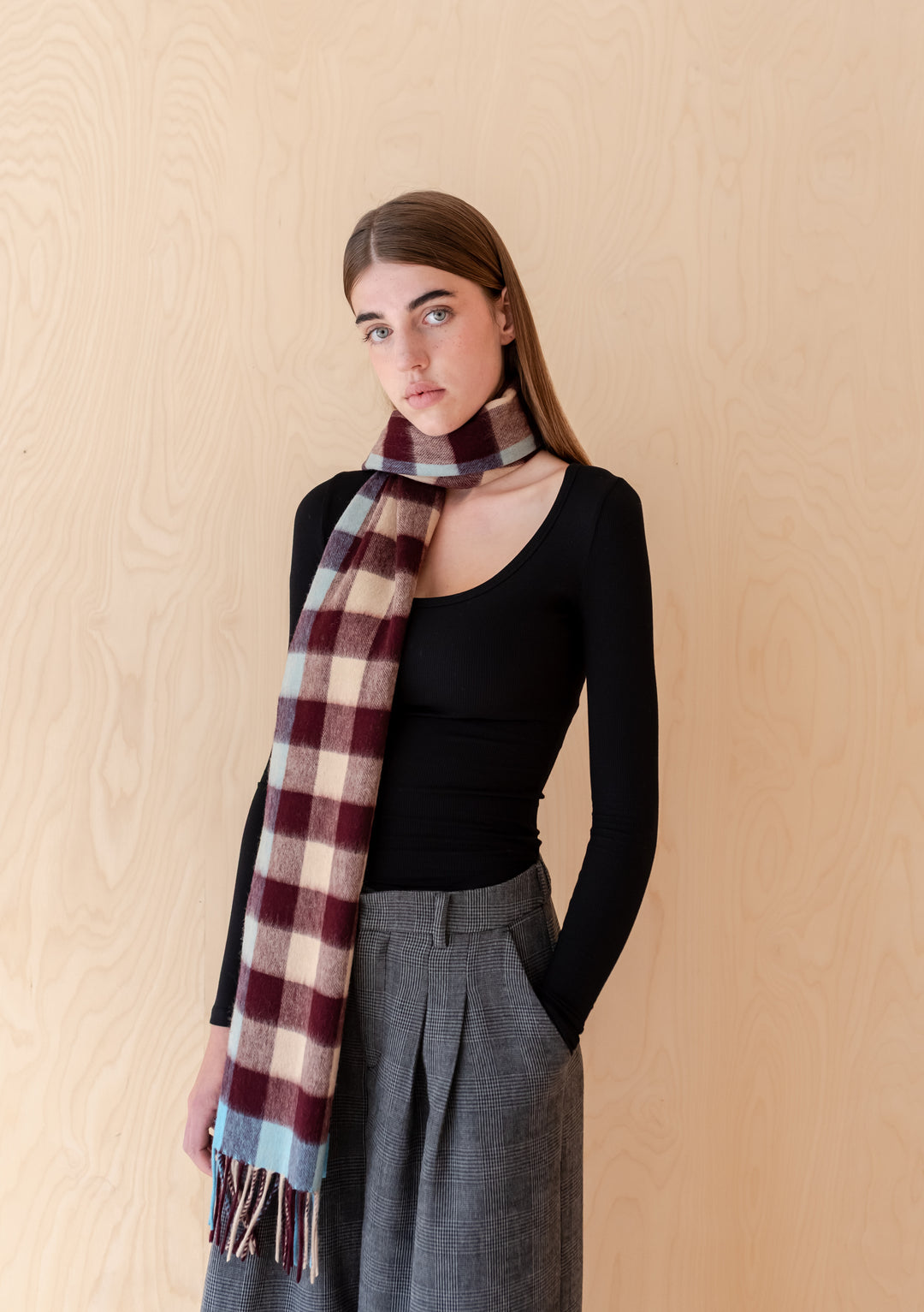 Woman wearing TBCo Lambswool Oversized Scarf in Camel Gingham with burgundy brown and blue check pattern against wood background