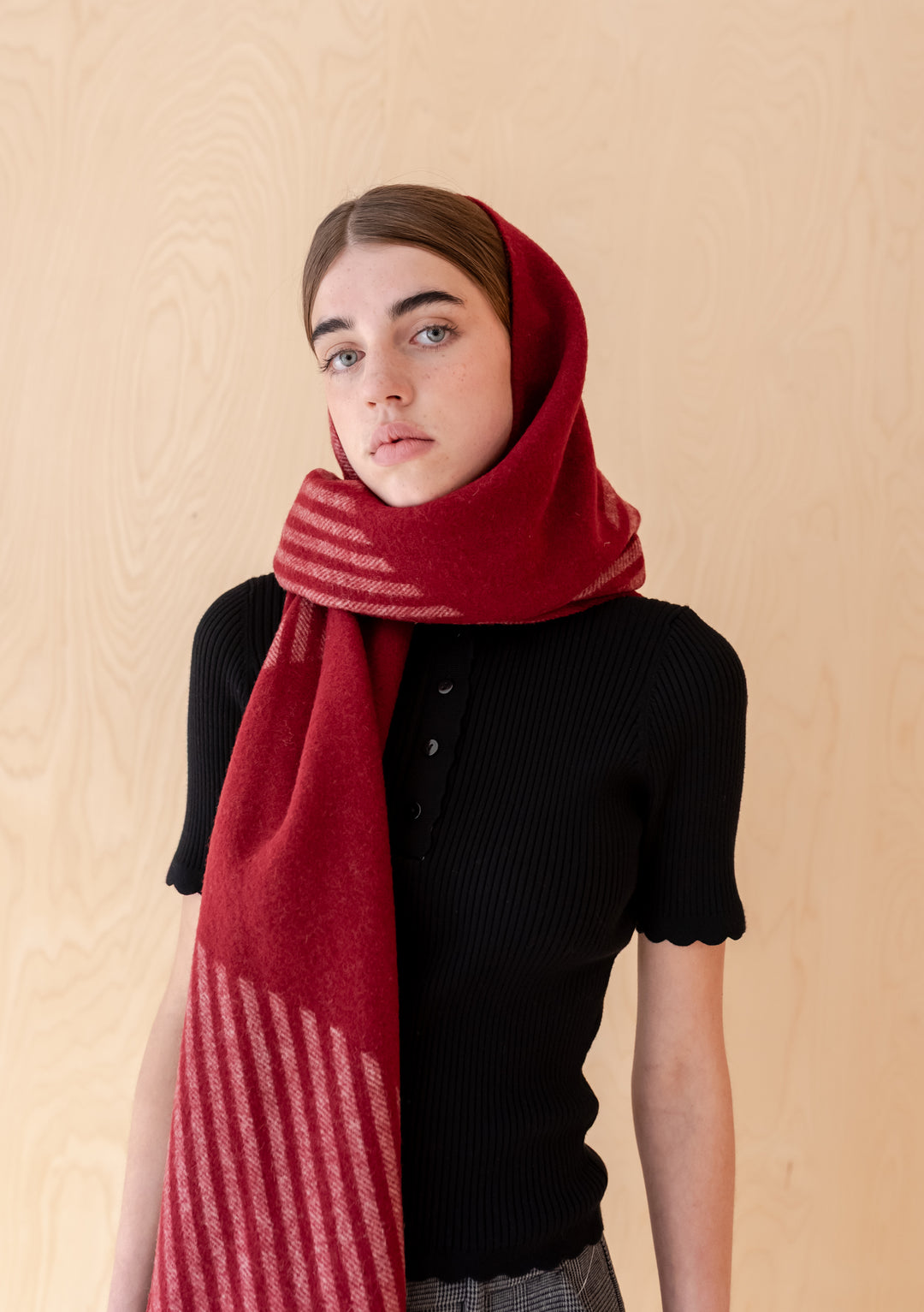 Woman wearing TBCo Lambswool Oversized Scarf in Burgundy Wave styled softly over a black top against wooden backdrop
