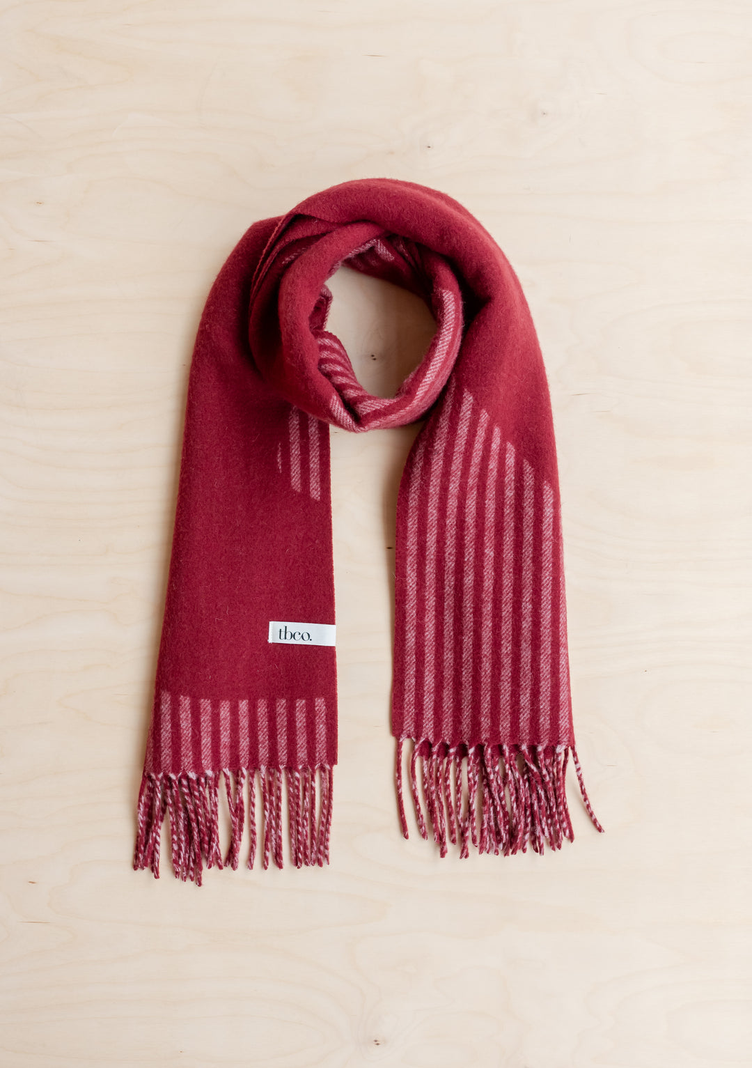 TBCo Lambswool Oversized Scarf in Burgundy Wave folded on light wood surface with fringed edges and striped pattern