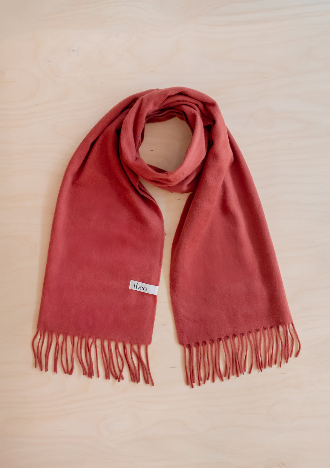 Lambswool Oversized Scarf in Mulberry by TBCo, soft lambswool with fringed edges laid flat on wood surface