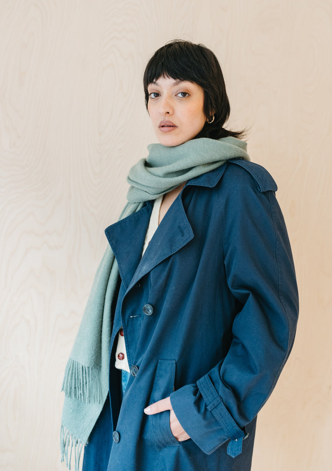 TBCo Lambswool Blanket Scarf in Sage Melange styled with navy trench coat, showcasing soft fringed wool texture and classic drape