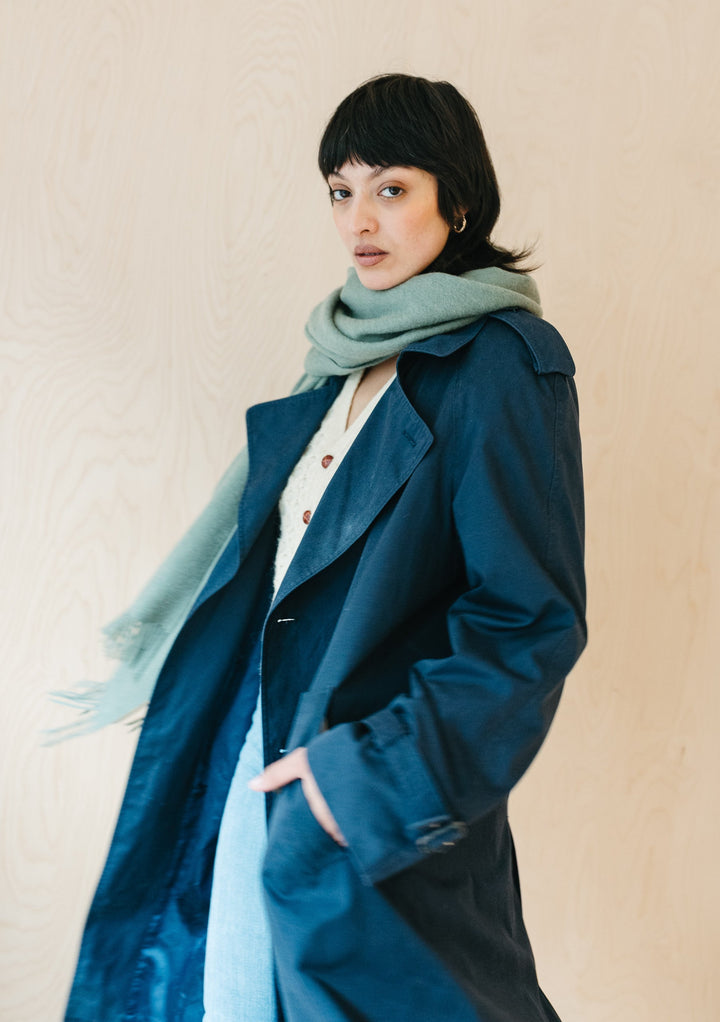 Model wearing TBCo Lambswool Blanket Scarf in Sage Melange draped elegantly with navy trench coat against neutral backdrop