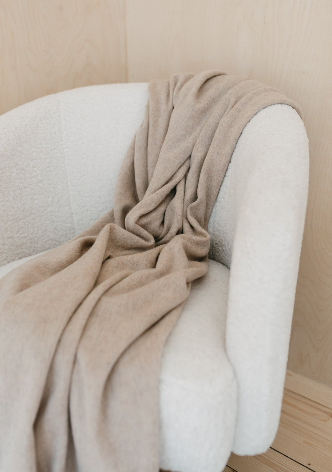 TBCo Lambswool Blanket in Oatmeal Melange draped elegantly over white armchair, showcasing soft texture and fringed edges