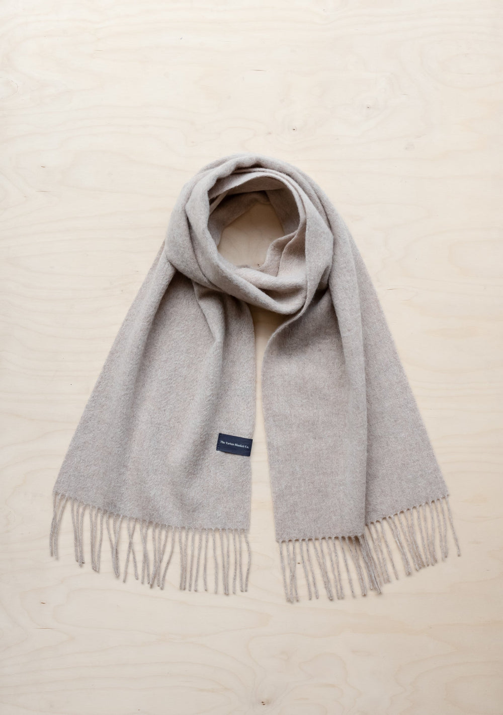 TBCo Lambswool Oversized Scarf in Oatmeal Melange with fringed ends, laid flat against cream background