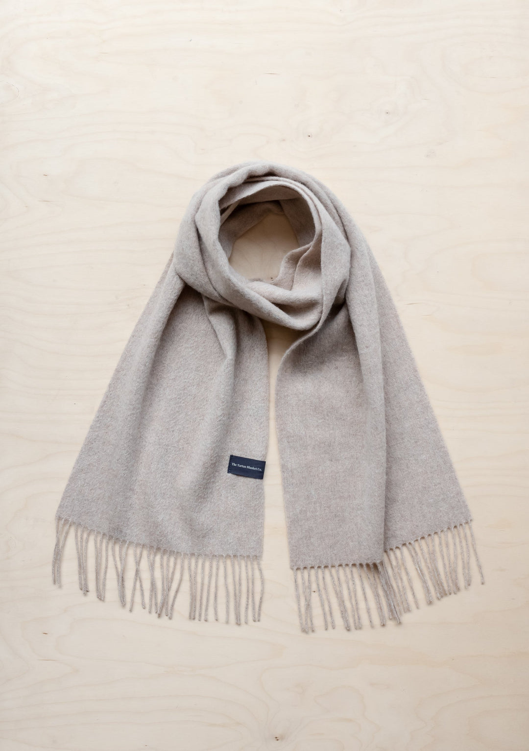 TBCo Lambswool Oversized Scarf in Oatmeal Melange with fringed ends, laid flat against cream background