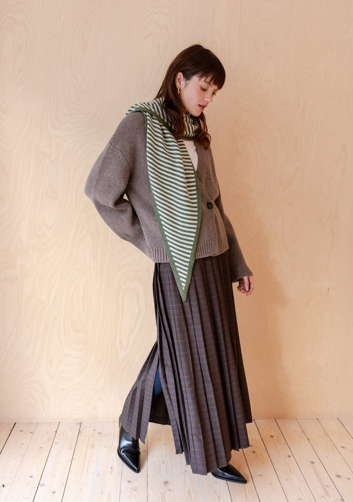 TBCo Large Merino Triangle Scarf in Green Stripe styled with grey cardigan and pleated maxi skirt against wooden backdrop