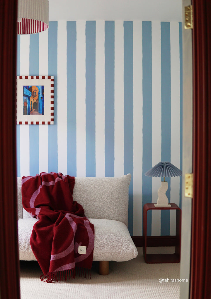 Lambswool Blanket in Red Wave Jacquard by TBCo draped on a white sofa in a stylish blue striped room.