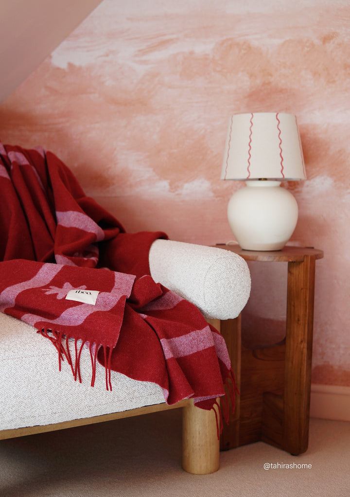 TBCo Lambswool Blanket in Red Wave Jacquard draped over a cream chair beside a wooden side table with lamp
