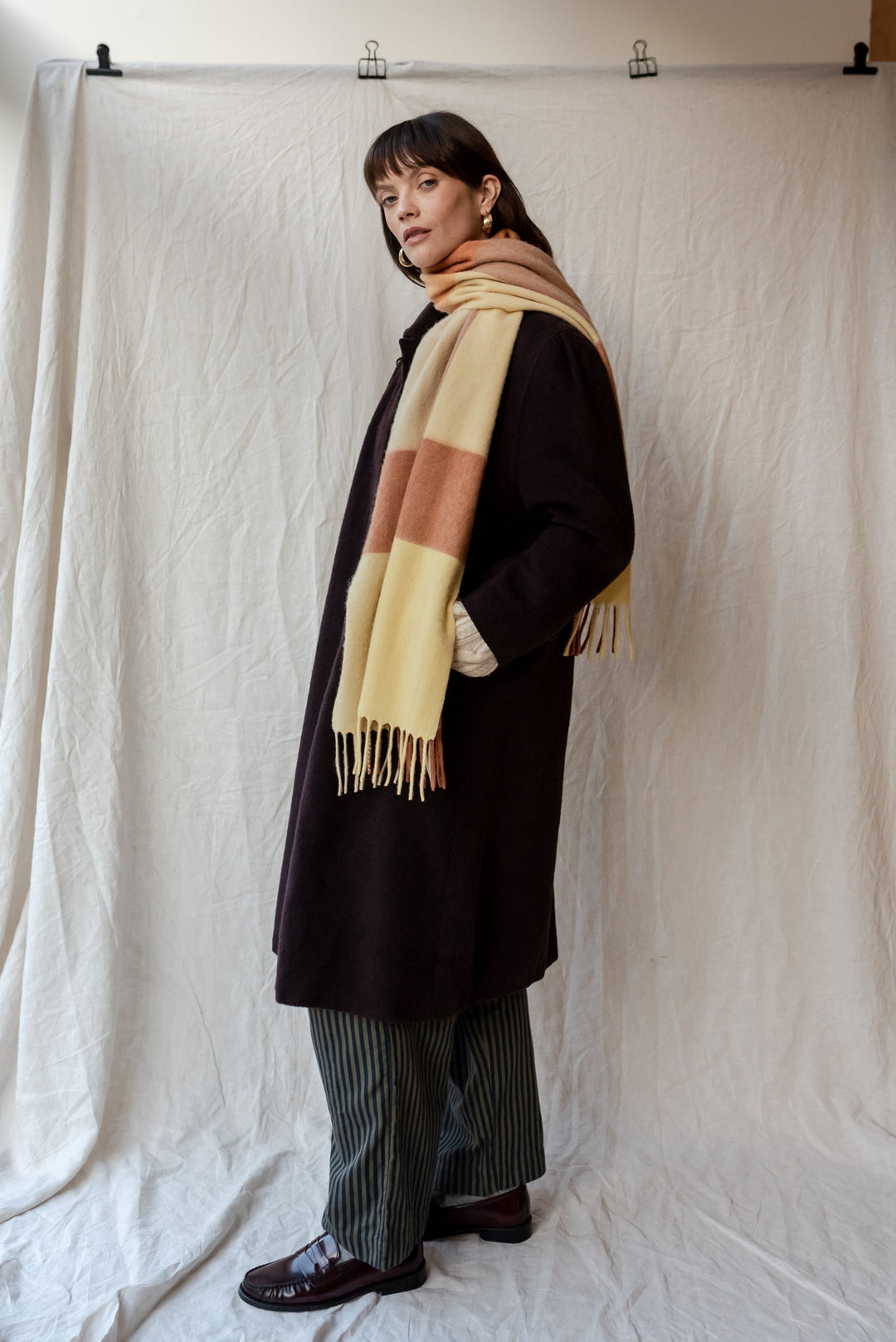 TBCo lambswool oversized scarf in buttermilk and brown block check pattern styled with black winter coat and striped trousers