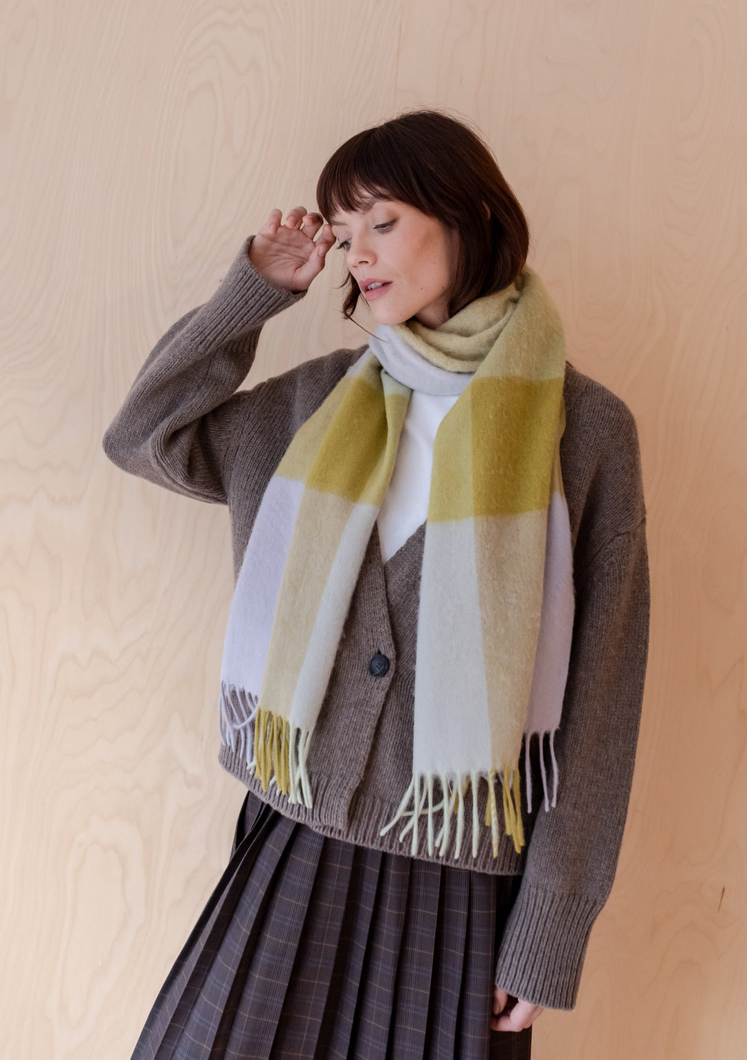 Soft lambswool TBCo oversized scarf in sage block check pattern, styled with grey cardigan against wooden backdrop