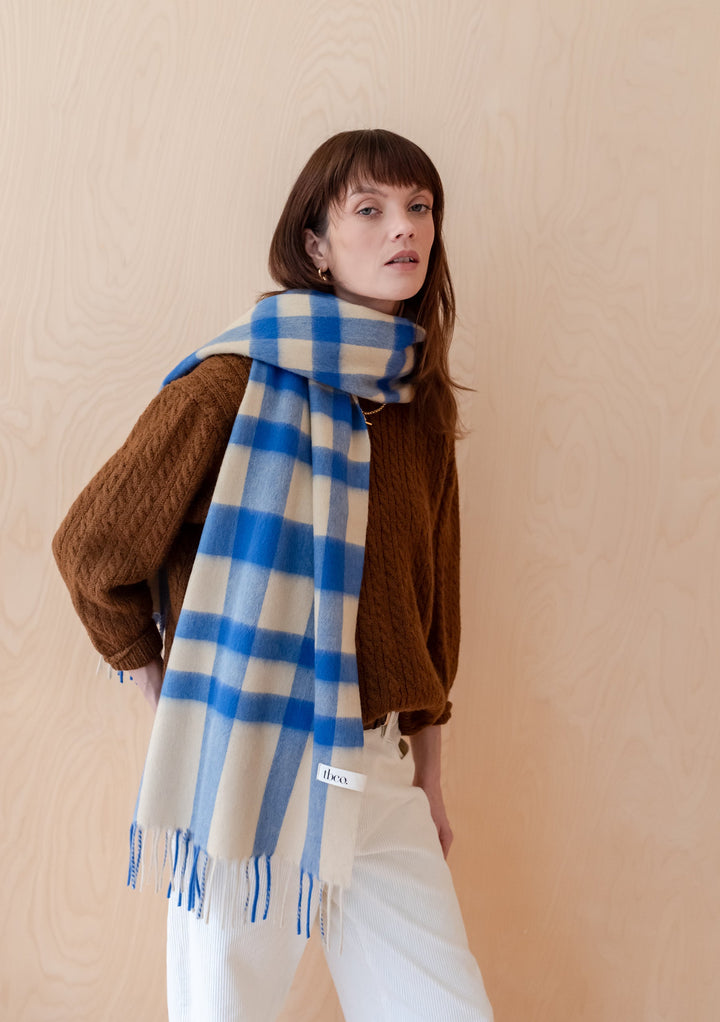 TBCo Lambswool Oversized Scarf in blue and cream check pattern, styled with brown knit jumper against beige backdrop