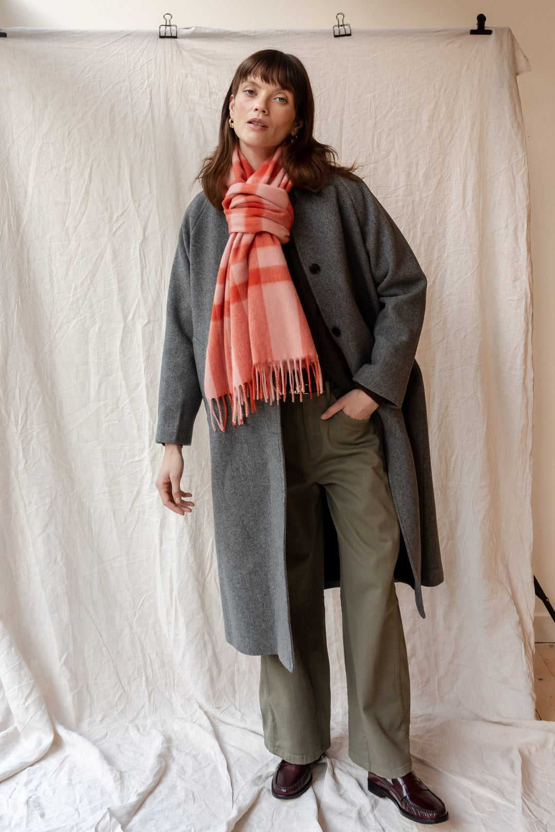 Pink check TBCo lambswool oversized scarf styled with grey wool coat and green trousers against white backdrop