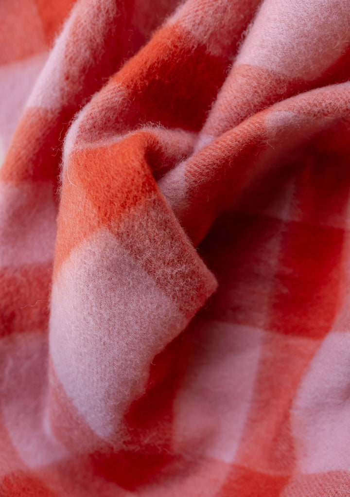 Close-up texture detail of TBCo lambswool oversized scarf in pink and red check pattern showing soft wool fibres
