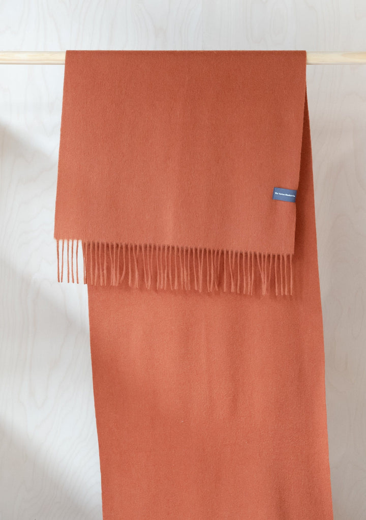TBCo Lambswool Oversized Scarf in Rust Melange displayed draped over wooden rail showing fringed ends and full length