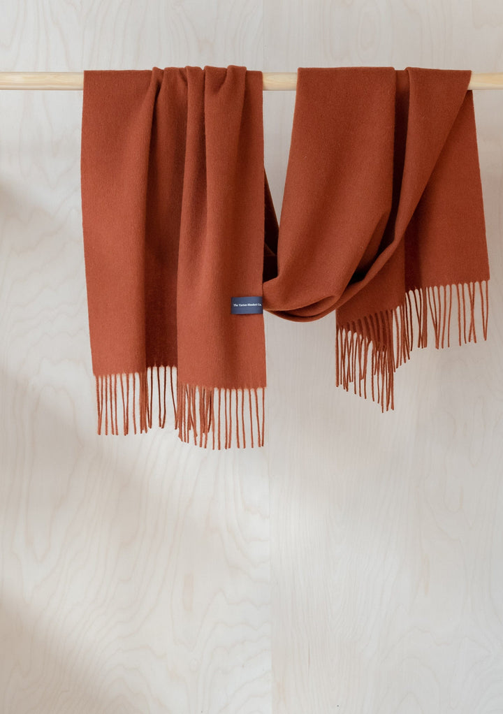 TBCo Lambswool Oversized Scarf in Rust Melange draped over wooden rail, showing soft texture and fringed ends