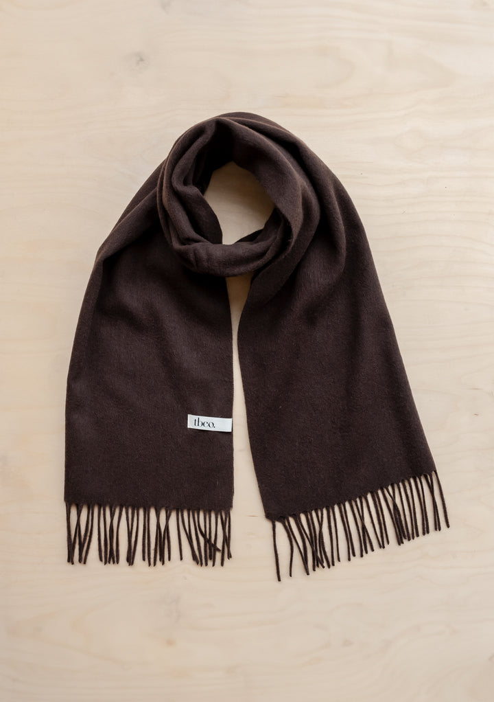TBCo lambswool oversized scarf in chocolate brown with fringed edges, styled flat against wooden surface