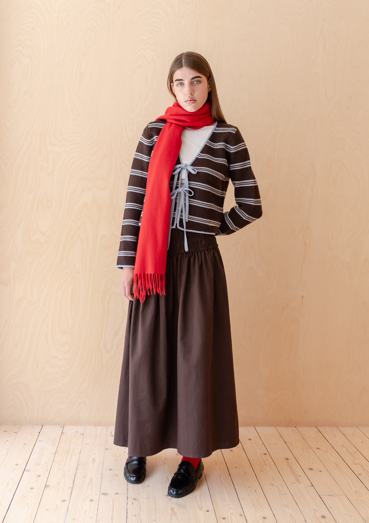 Model wearing TBCo Lambswool Oversized Scarf in Red, styled with a striped cardigan and long skirt against pale wood background