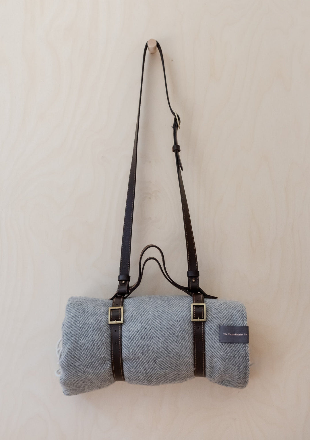 TBCo Leather Picnic Carrier with brown leather straps and adjustable shoulder strap holding grey herringbone wool blanket