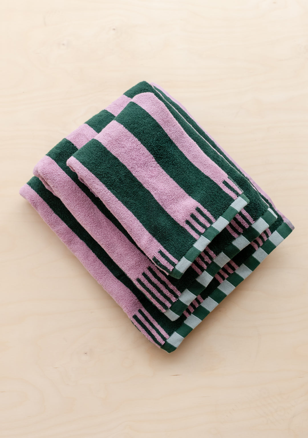 Stacked TBCo Terry Cotton Towels in Rose Stripe with pink and dark green stripes and checkerboard edges on wood surface