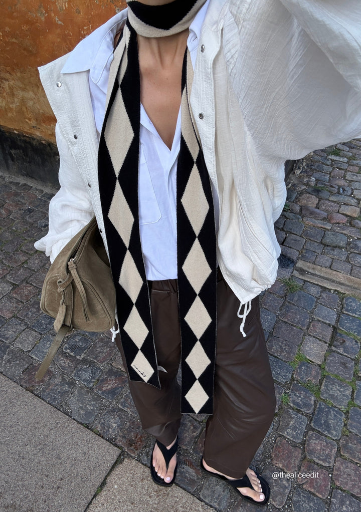 Person wearing TBCo Merino Wool Skinny Scarf in Black Harlequin with diamond pattern and casual outfit outdoors